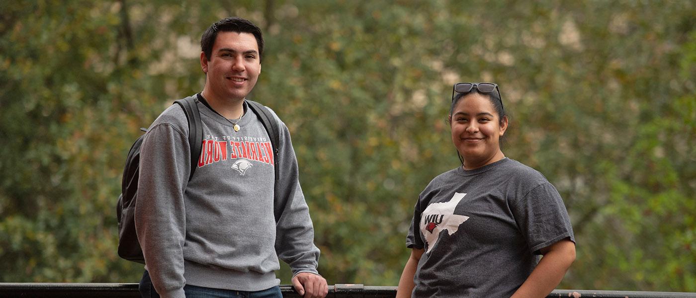 Two smiling students standing outside with trees in the background